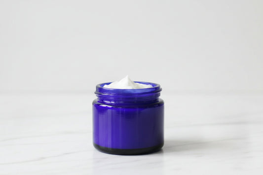 A small open jar of white tallow cream  in a cobalt blue glass container, placed on a marble surface.